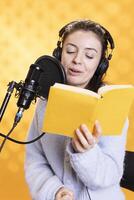 Cheerful lady narrating book word for word to produce audiobook. Joyous narrator using storytelling skills to engage audience while producing digital recording of novel, studio background photo