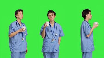 Medical assistant drinking cup of coffee before starting exam appointments in the morning, enjoying caffeine refreshment against greenscreen backdrop. Nurse drinks beverage. Camera B. photo