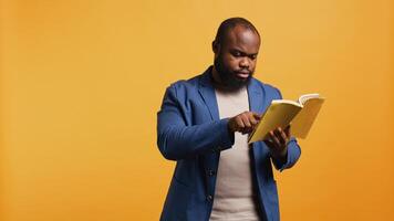 Man struggling to read book with small font, pointing finger to words on page. Person enjoying literature novel, wetting fingers to change page, isolated over studio background, camera B photo