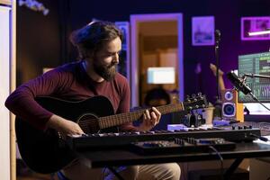 Audio engineer playing new tunes on acoustic instrument and using daw software to record music, adding sound effects to his songs. Songwriter composing music with guitar and mixing console. photo