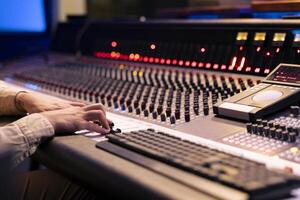 Audio engineer twisting pre amp knobs and switchers on panel board in control room, using mixing console for editing and mastering music. Professional skilled producer in music studio. photo