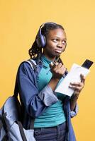 African american student thinking how to write homework while listening music, studio background. Studious girl learning for school exam, repeating information and enjoying songs on headphones photo