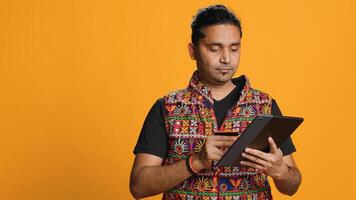 Man adding payment method on shopping website using tablet, taking advantage of promotions, studio background. Indian person buying stuff online using credit card, typing data on device, camera A photo