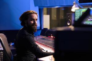 Portrait of sound designer working with mixing console and daw software on pc in professional studio, producing tracks for a pop album. Talented producer editing new music in control room. photo