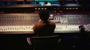 African american music producer finishing his new track in professional studio, recording and editing a song in post production. Skilled audio engineer mixing and mastering tunes. Camera B. photo