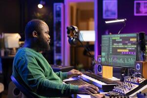 African american composer creating a new track for a project, using professional production pc interface in his home studio. Creative artist songwriter producing music with sound effects. photo