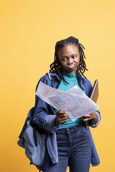 African american employee displeased with too much work, browsing though marketing report pages, studio background. Irked worker reading paperwork containing economic graphs and figures photo