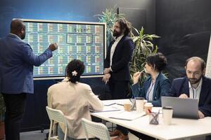 Team of business specialists following stock trade values on interactive board, developing a new financial strategy to increase capital. Forecast affiliates working on organizational success. photo