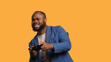 Portrait of cheerful BIPOC man playing videogames holding controller, studio background. Gamer smiling, having fun by participating in PvP online multiplayer game using console system, camera A photo