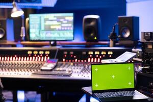 Young technician recording music on control desk next to mockup laptop, working on mixing console to produce new songs. Sound engineer creating tracks and editing in professional studio. photo