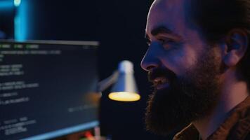 Joyous remotely working programmer in home office doing coding on computer at desk. Upbeat teleworking IT professional in apartment writing lines of code at workstation, camera B close up shot photo