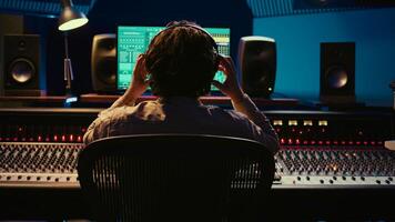 Sound designer working on track recording with audio professional software, operating technical equipment on panel board in control room. Audio engineer enhances music high quality. Camera B. photo
