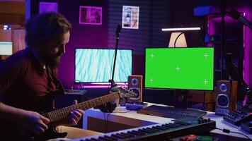 Male singer learning to play a new song on acoustic guitar, using greenscreen on computer to watch online tutorials. Artist songwriter practicing with his instrument in home studio. Camera B. photo