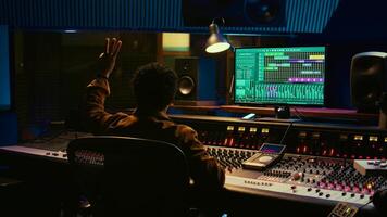 African american audio engineer counting down singer in sound booth, preparing to record and process tracks in control room. Producer twisting knobs and faders to enhance tune quality. Camera B. photo