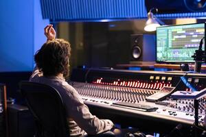 Sound designer counting down for singer in vocal booth to start performance for recording session, producing new music in control room. Skilled audio engineer operating panel board. photo