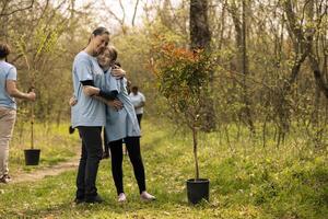 Portrait of mother and child protecting the natural ecosystem by planting trees with team of volunteers. People cultivating consciousness by restoring forest ecosystem with greenery and vegetation. photo