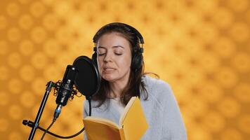 Voice actor reading book, recording for audiobook production using microphone and headset, studio background. Person using mic and headphones to produce digital recording of novel, camera A photo
