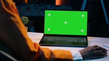 African american girl working with device showing greenscreen layout, sitting at desk and looking at chromakey display. Young woman using laptop with copyspace mockup template. Camera A. photo