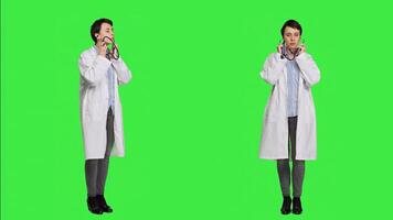 General practitioner with a white coat using stethoscope in studio, preparing to examine patients at checkup appointments. Female doctor in uniform standing against greenscreen backdrop. Camera A. photo