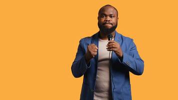 Aggressive lecturer holding motivational speech using microphone, gesturing with hands, isolated over studio background. Speaker urging spectators to take action, doing speech using mic photo