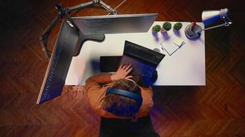Top down view of engineer typing code in home office, using Java programming language to develop software application. It specialist using multimonitor PC setup and laptop to finish tasks, aerial shot photo