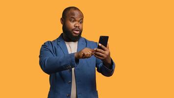 Smiling african american man greeting friends during teleconference meeting using smartphone, studio background. Friendly person waving hand, saluting mate during internet call, camera A photo