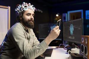 Smiling programmer wearing EEG headset holding disk containing software turning AI sentient, satisfied with finished product. Happy developer with cartridge able to awake artificial intelligence photo