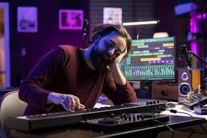 Tired artist losing sleep to learn new piano notes in home studio, playing midi controller electronic keyboard to compose songs. Producer being exhausted and stresses while he works on music. photo
