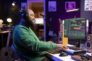 Sound technician playing piano notes to edit with DAW software in his home studio, working at night on producing new songs with electronic synthesizer. Producer composing tracks on midi controller. photo