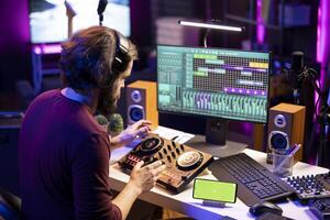 Audio engineer following online tutorial on smartphone greenscreen display, learning to use mixing console and add sound effects on songs. Producer creating soundtracks on daw software. photo