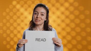 Woman holding message in hands urging people to read more, talking about importance of lecture, isolated over studio background. Bookworm promoting literacy concept, camera B photo