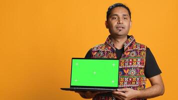 Upbeat tech specialist doing promotion using isolated screen laptop, studio background. Cheerful indian person holding chroma key notebook, doing advertisement for it, camera A photo