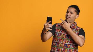 Joyous Indian man greeting friend over online videocall on cellphone, doing friendly gestures. Excited person bonding with mate using mobile phone videoconference, studio background, camera A photo