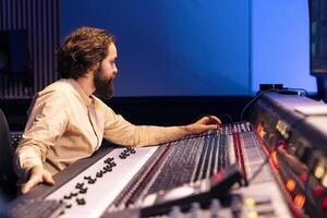 Mixing engineer presses faders and control desk buttons to enhance sound quality on recordings, working on new album. Technical expert balancing tracks and adding effects, stereo gear. photo