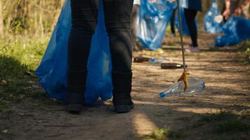 Diverse activists group using claw tools to grab trash and plastic, storing it in garbage disposal bags. People gathering to collect rubbish and recycling for sustainable lifestyle. Camera A. photo
