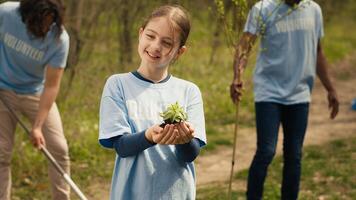 Little girl holding a small green sprout with natural soil in order to preserve forest habitat and protect the ecosystem. Child growing up with a dedication for environmental protection. Camera A. photo