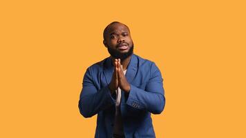 Friendly african american man puts hands together in apology gesture, asking for forgiveness. Apologetic BIPOC man doing sorry gesturing, asking for pardon, isolated over studio background, camera B photo