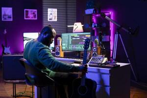 Producer composing new music on acoustic instrument in home studio, using a microphone to sing the chords. Musician songwriter works with mixing console and mixing software, guitarist producing tunes. photo