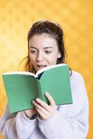 Woman gasping while reading intriguing book, feeling surprised, enjoying hobby during leisure time. Amazed person astounded by novel story plot twists, isolated over studio background photo