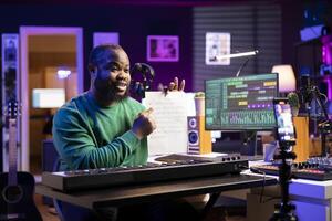 Young songwriter explaining music sheet with notes on online master class vlog, hosting internet lessons in his home studio. Artist composer teaching people how to sing on midi controller instrument. photo