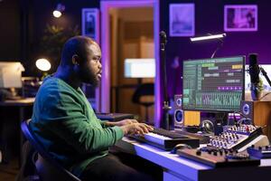 Creative songwriter recording new tracks with microphone and midi controller, playing piano notes in home studio. Skilled musician artist composing music with electronic keyboard and stereo gear. photo