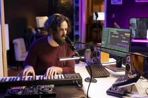 Creative musician recording new tunes with microphone and midi controller, playing piano keys in home studio. Skilled composer producing music with modern electronic keyboard and audio gear. photo