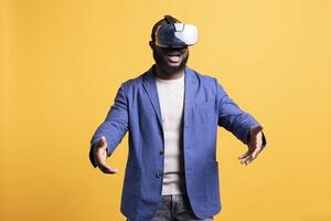 Happy tech fan wearing virtual reality goggles, pretending to hold something. Joyful man delighted to use modern technology VR headset, making tactile hand gesturing, studio background photo
