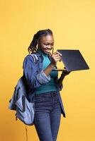 Joyful BIPOC teenager opening laptop, preparing to start job shift, isolated over studio background. Jolly african american girl with notebook ready to do business related tasks on it photo