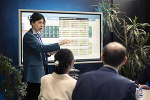 Office manager presenting data analysis and funding on interactive board, deliberating on income and revenue growth with her affiliates. Accomplishing financial objectives in the organization. photo