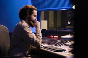 Sound engineer mixes individual tracks to create balanced music after audio recording session in professional studio. Producer creating music, editing tracks with mixing console and sliders. photo