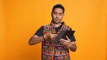 Man adding payment method on shopping website using tablet, taking advantage of promotions, studio background. Indian person buying stuff online using credit card, typing data on device, camera B photo