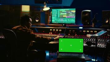 African american artist working with mockup on display in control room, mixing and mastering tracks with audio console and buttons or knobs. Music producer recording and editing sounds. Camera B. photo