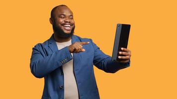 African american man having funny conversation with friends during teleconference meeting using tablet, studio background. Person laughing, having fun with mates during internet videocall, camera A photo