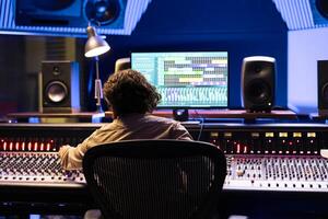 Skilled audio engineer operating on digital computer software, editing music with mixing console and control desk. Technician specialist producing tracks with sliders and switchers in studio. photo
